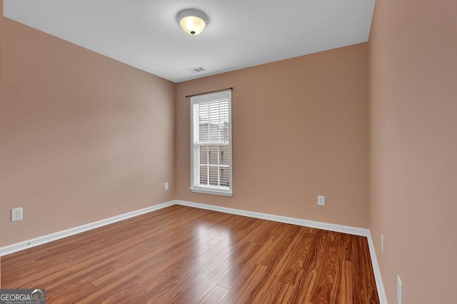 empty room with wood finished floors, visible vents, and baseboards