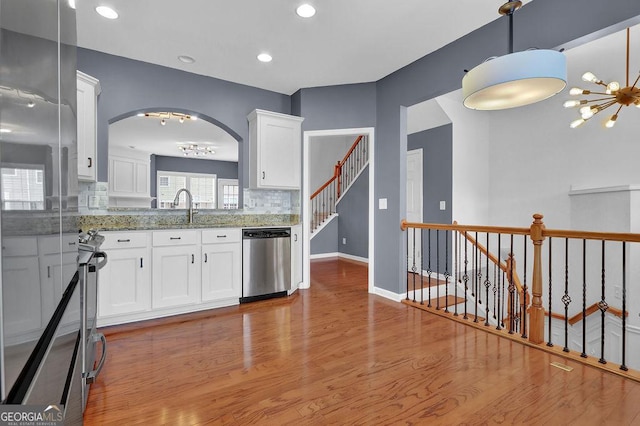 kitchen featuring light wood finished floors, light stone countertops, stainless steel appliances, an inviting chandelier, and white cabinetry