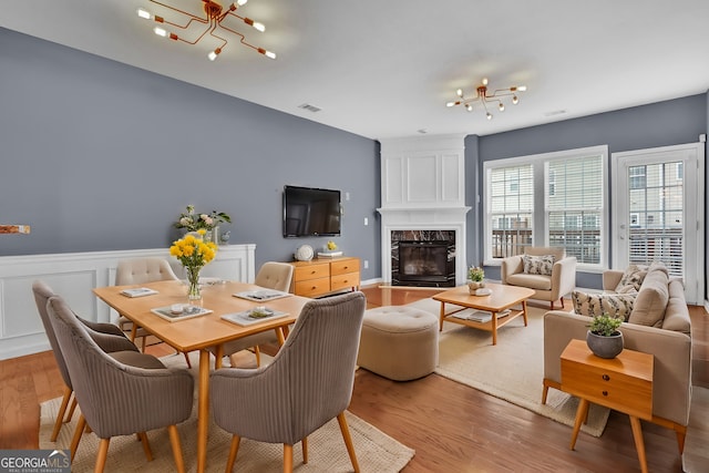 dining area with visible vents, a chandelier, light wood-type flooring, wainscoting, and a fireplace