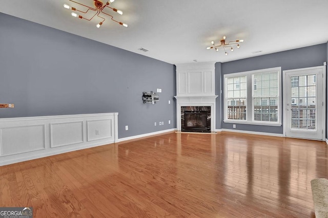 unfurnished living room with visible vents, a premium fireplace, an inviting chandelier, wood finished floors, and a decorative wall