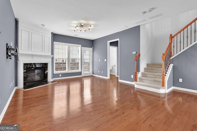 unfurnished living room with a fireplace, stairway, wood finished floors, and baseboards