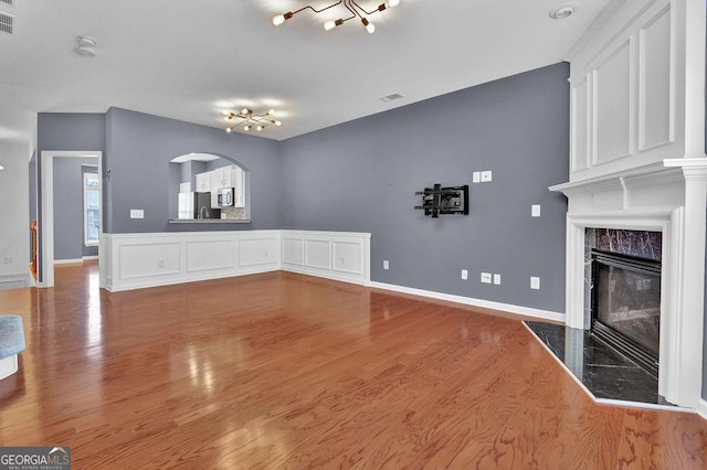 unfurnished living room featuring visible vents, wood finished floors, arched walkways, a premium fireplace, and baseboards