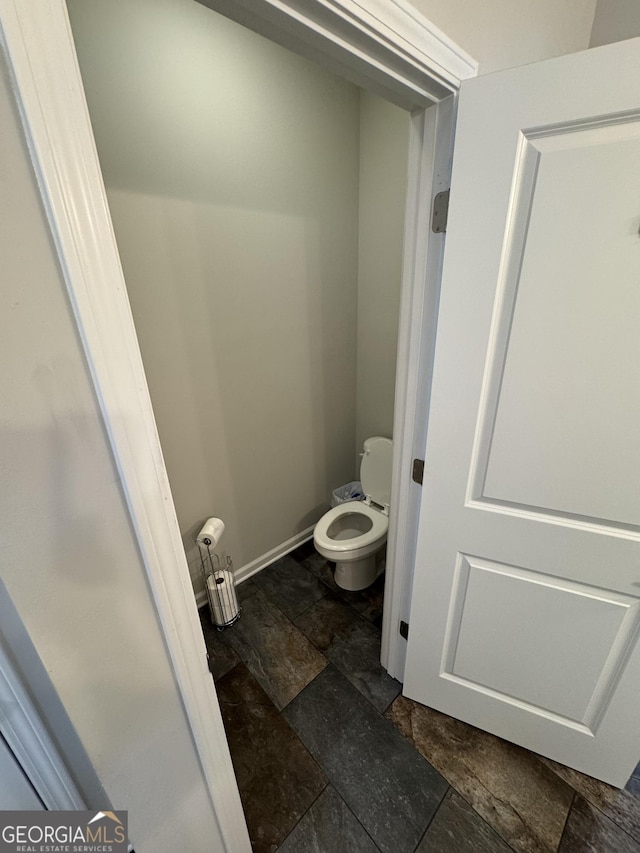 bathroom with stone tile floors, toilet, and baseboards