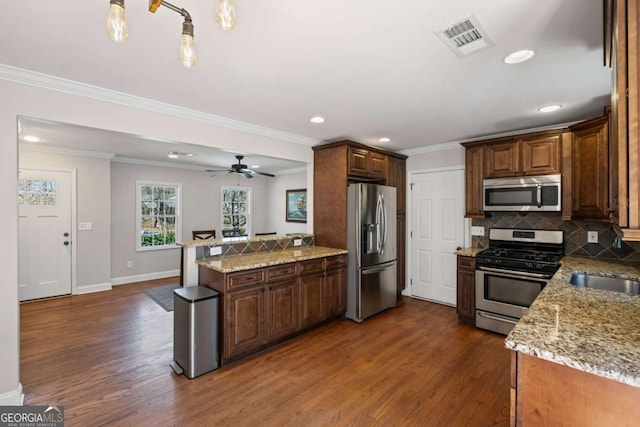 kitchen featuring visible vents, a peninsula, decorative backsplash, dark wood-type flooring, and appliances with stainless steel finishes