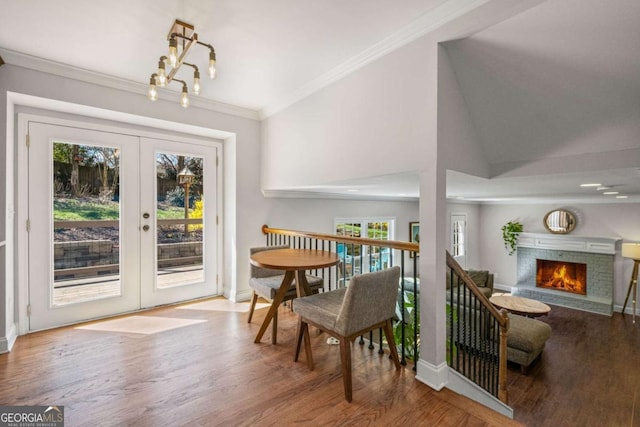 dining room featuring wood finished floors, french doors, crown molding, baseboards, and a brick fireplace