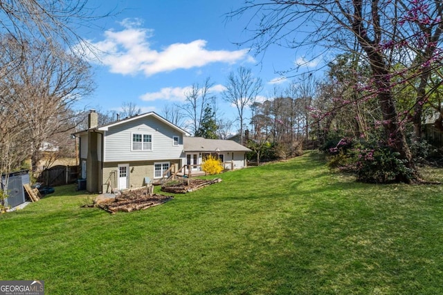 rear view of house with a lawn, a chimney, and fence