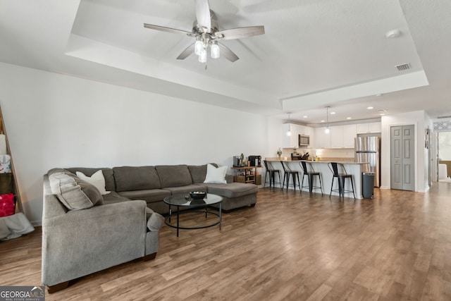 living room featuring wood finished floors, visible vents, recessed lighting, ceiling fan, and a raised ceiling