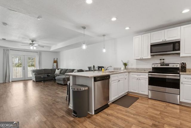 kitchen with white cabinets, appliances with stainless steel finishes, light wood-type flooring, and a peninsula