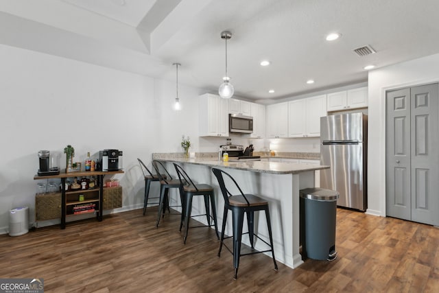 kitchen featuring a breakfast bar area, visible vents, a peninsula, appliances with stainless steel finishes, and white cabinetry