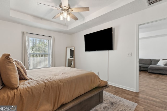 bedroom with visible vents, baseboards, wood finished floors, a raised ceiling, and a ceiling fan