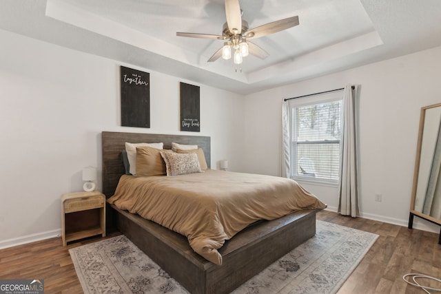 bedroom featuring a tray ceiling, wood finished floors, and baseboards