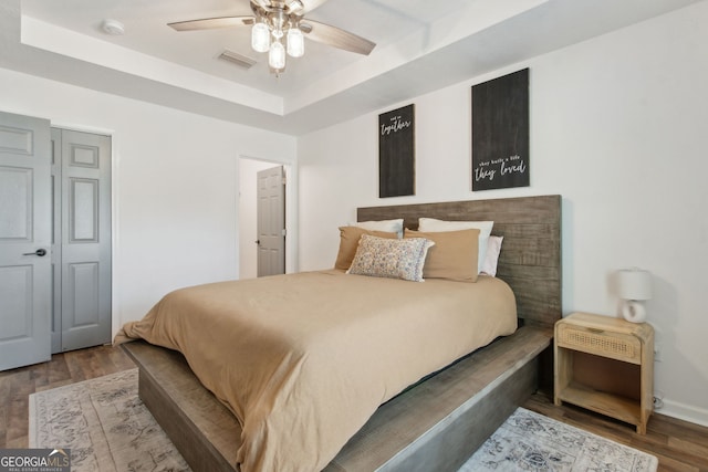 bedroom with visible vents, ceiling fan, a tray ceiling, and wood finished floors