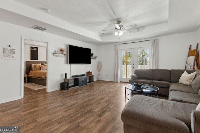 living area with visible vents, baseboards, a tray ceiling, wood finished floors, and a ceiling fan