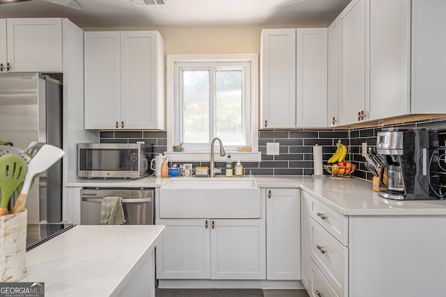 kitchen featuring a sink, decorative backsplash, appliances with stainless steel finishes, and white cabinetry