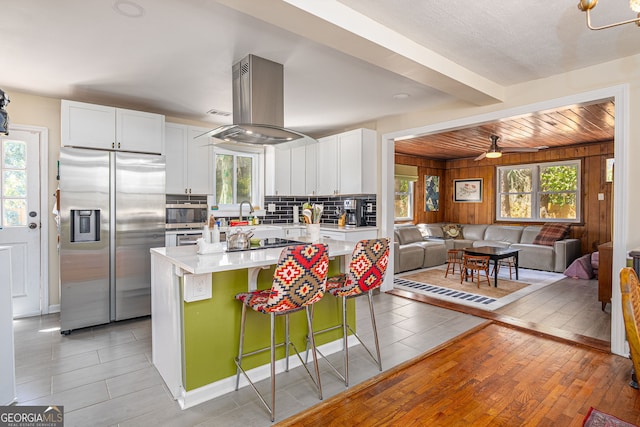 kitchen featuring island exhaust hood, light countertops, white cabinets, appliances with stainless steel finishes, and tasteful backsplash