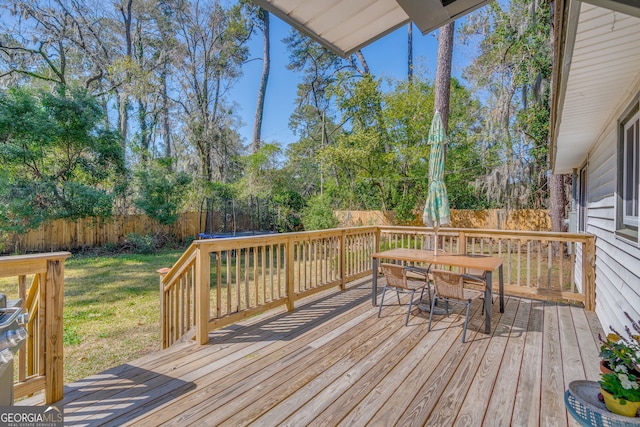 deck with outdoor dining space, a trampoline, a fenced backyard, and a lawn