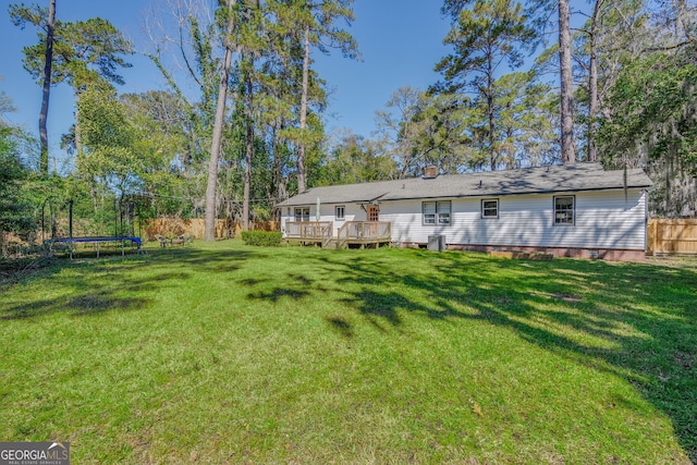 view of yard featuring a deck, a trampoline, fence, and central AC