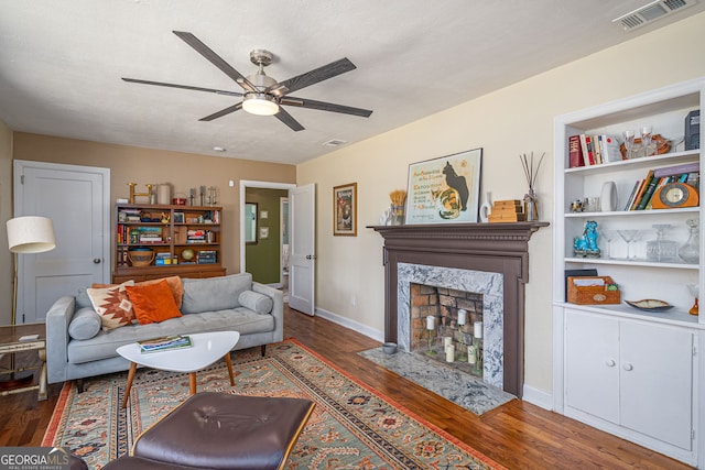 living area featuring wood finished floors, a ceiling fan, visible vents, baseboards, and a fireplace