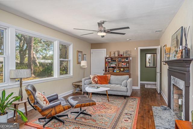 living room featuring a ceiling fan, visible vents, baseboards, a fireplace, and hardwood / wood-style flooring