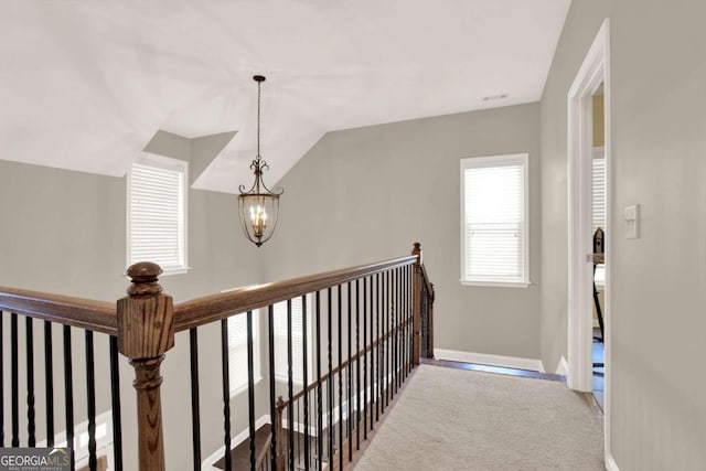 hall featuring baseboards, carpet, vaulted ceiling, an upstairs landing, and an inviting chandelier