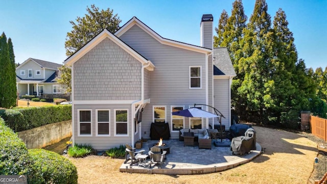 rear view of property featuring a chimney, an outdoor living space with a fire pit, a patio, and fence