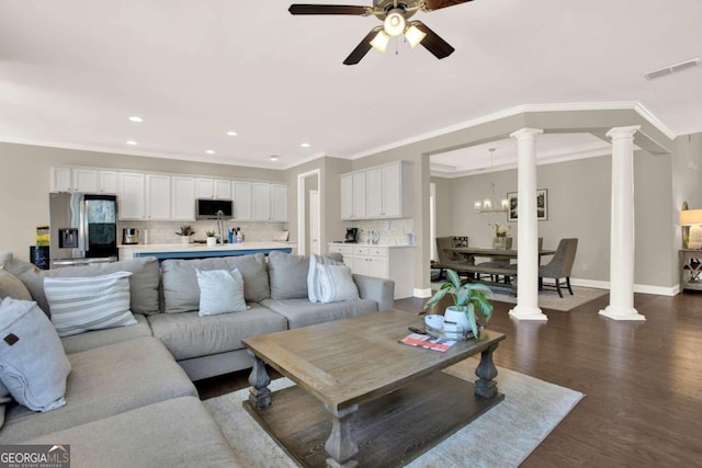 living room featuring visible vents, baseboards, decorative columns, dark wood-style flooring, and ceiling fan with notable chandelier