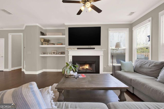 living room featuring visible vents, crown molding, a warm lit fireplace, wood finished floors, and a ceiling fan