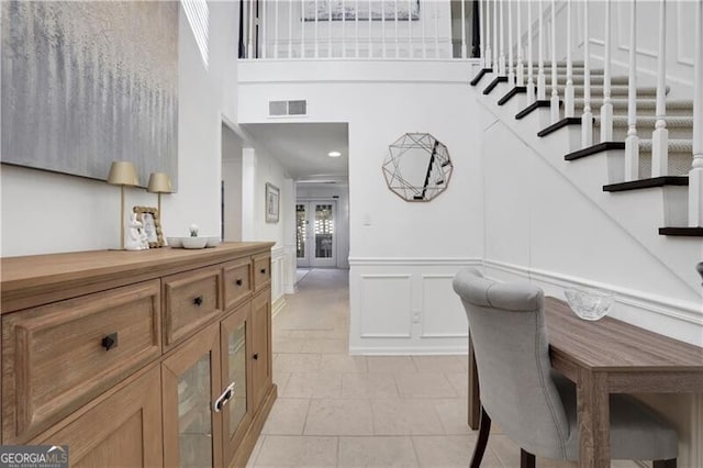 interior space featuring visible vents, a wainscoted wall, a decorative wall, a towering ceiling, and stairs