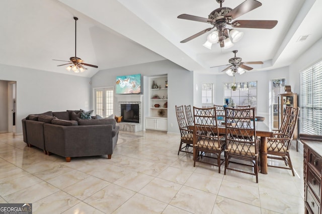 dining space with visible vents, built in shelves, ceiling fan, a tray ceiling, and a tile fireplace