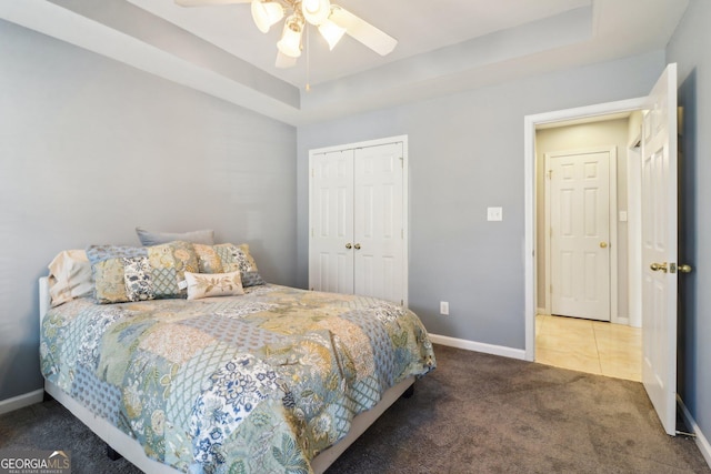 carpeted bedroom featuring a ceiling fan, a tray ceiling, baseboards, and a closet