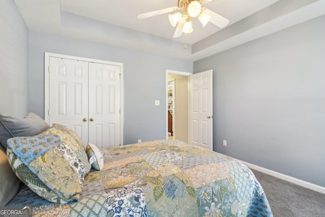 bedroom with a closet, carpet flooring, baseboards, and a tray ceiling