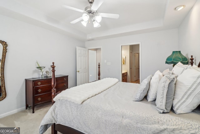 bedroom with baseboards, light carpet, ensuite bathroom, a raised ceiling, and a ceiling fan