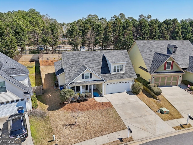 traditional-style house with an attached garage, roof with shingles, driveway, and fence