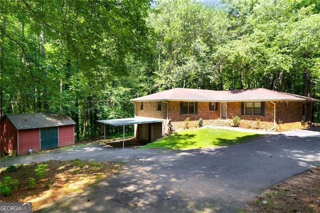 ranch-style house featuring a detached carport, a front yard, a wooded view, and driveway