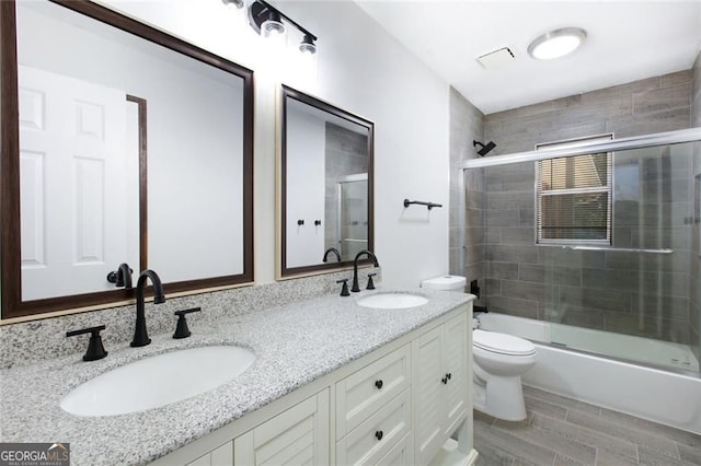 full bath with double vanity, toilet, shower / bath combination with glass door, and a sink