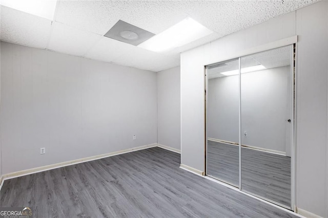 unfurnished bedroom with a drop ceiling, baseboards, a closet, and wood finished floors