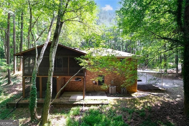 exterior space with a patio area, brick siding, a wooded view, and a sunroom