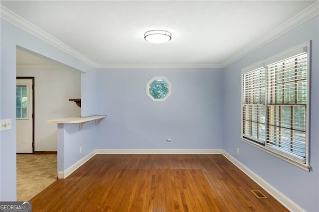 spare room with crown molding, wood finished floors, baseboards, and visible vents