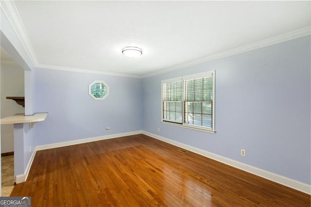 spare room featuring crown molding, wood finished floors, baseboards, and visible vents