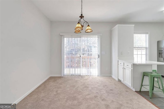 unfurnished dining area featuring a chandelier, baseboards, and carpet floors