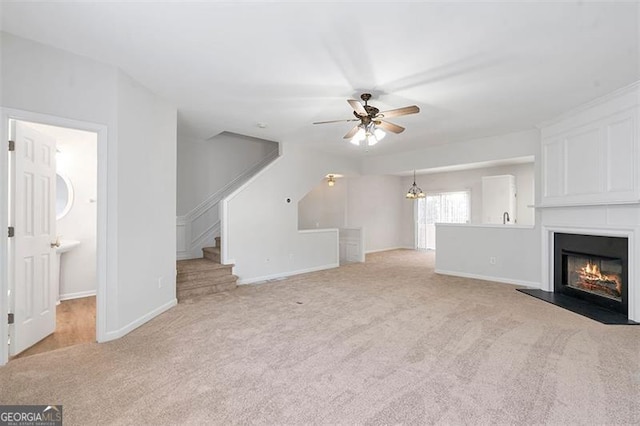 unfurnished living room with ceiling fan with notable chandelier, a glass covered fireplace, carpet floors, baseboards, and stairs