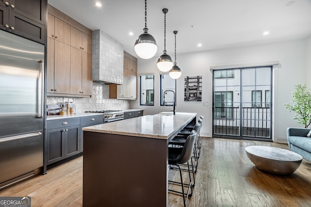 kitchen with an island with sink, light stone countertops, high quality appliances, light wood-style flooring, and a breakfast bar area