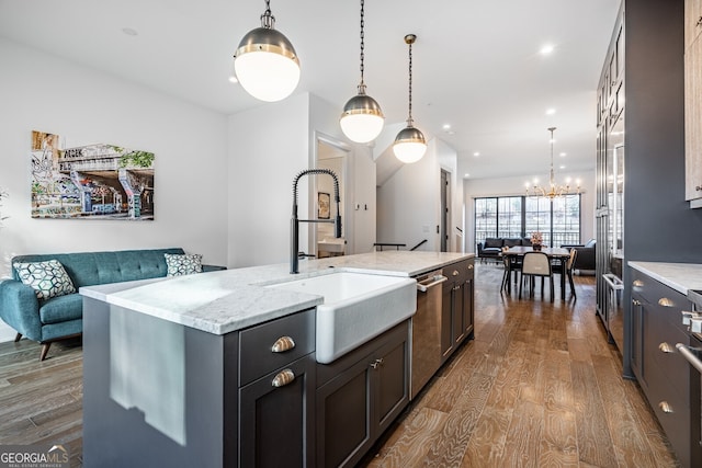kitchen with stainless steel dishwasher, a sink, a center island with sink, a notable chandelier, and wood finished floors