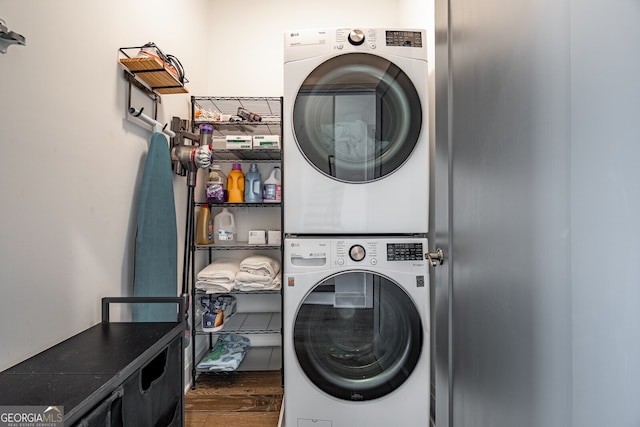 clothes washing area featuring stacked washing maching and dryer, wood finished floors, and laundry area