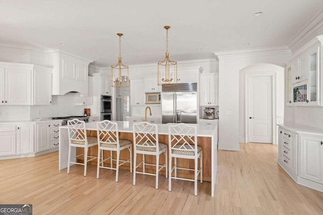 kitchen with a sink, light countertops, light wood-style floors, built in appliances, and a kitchen breakfast bar