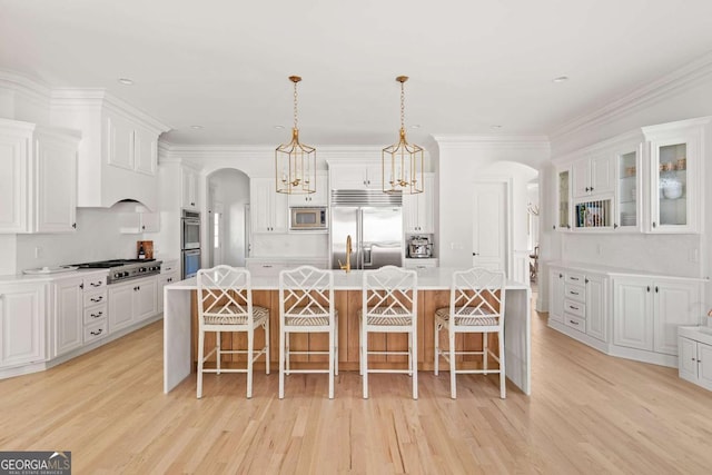 kitchen featuring a kitchen bar, light countertops, arched walkways, and built in appliances