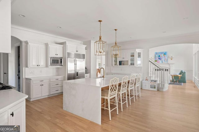 kitchen with a breakfast bar area, arched walkways, light countertops, light wood-style floors, and built in appliances