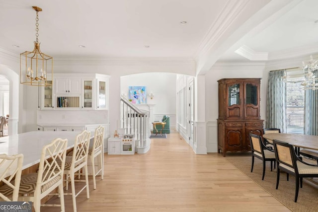 dining space featuring arched walkways, light wood-style floors, wainscoting, a decorative wall, and a chandelier