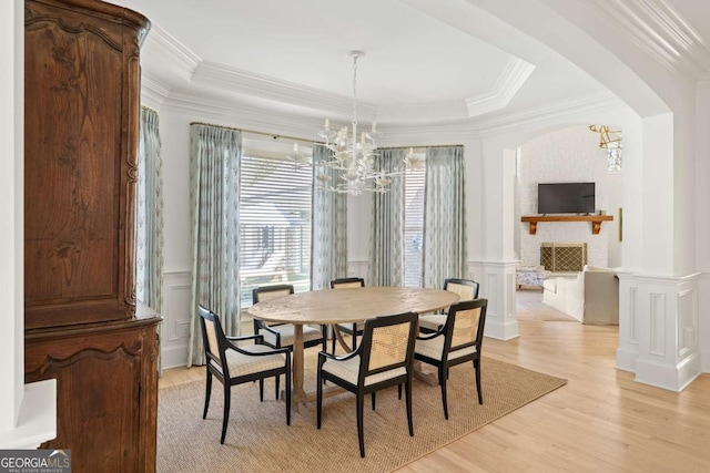 dining space featuring light wood finished floors, a notable chandelier, crown molding, and a decorative wall