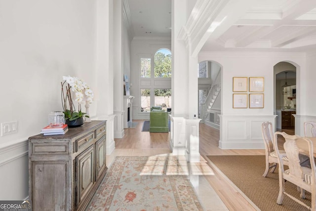 foyer with ornamental molding, beam ceiling, arched walkways, a decorative wall, and coffered ceiling